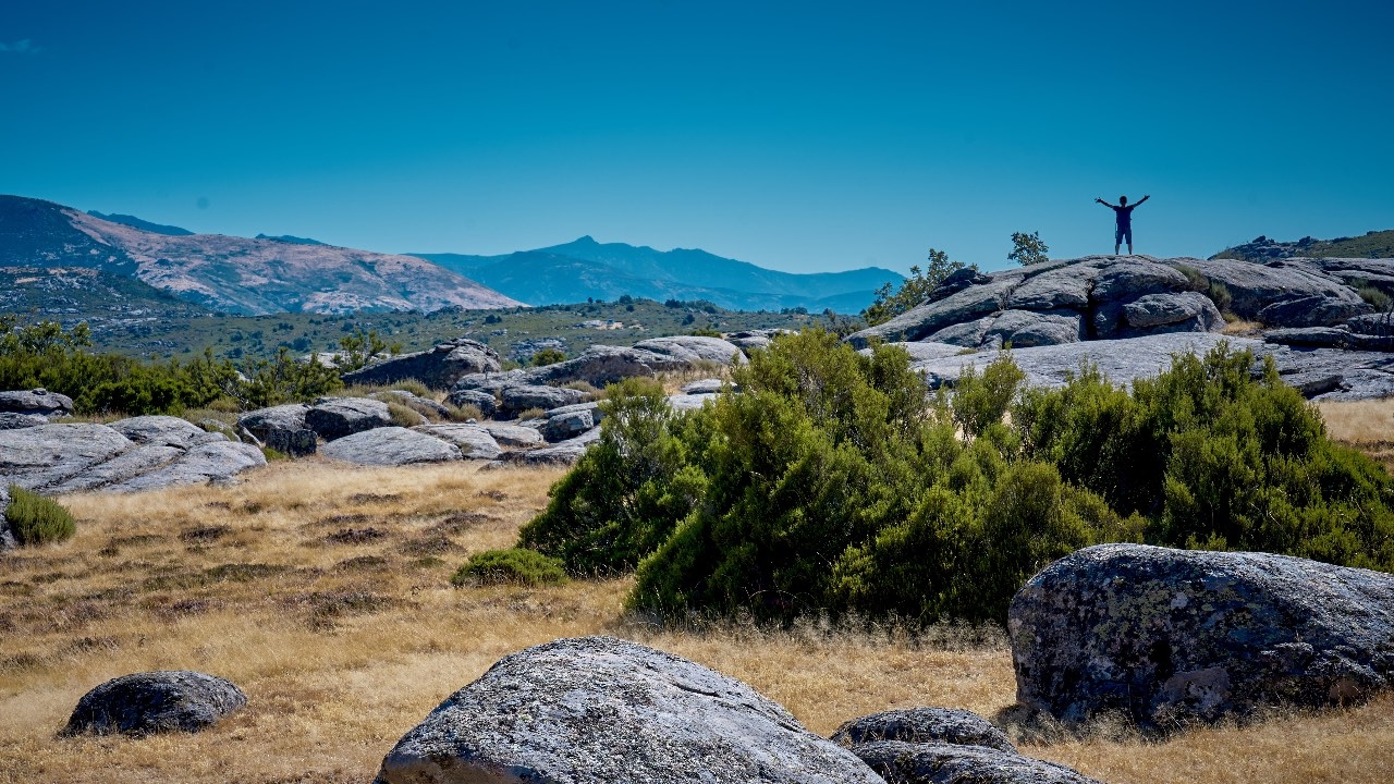 Paisaje donde se ve a una persona a lo lejos subido a una roca y con los brazos en alto