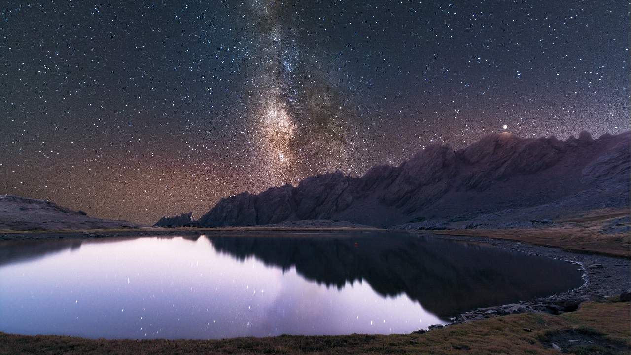 paisaje de un cielo estrellado con un lago y una montaña al fondo