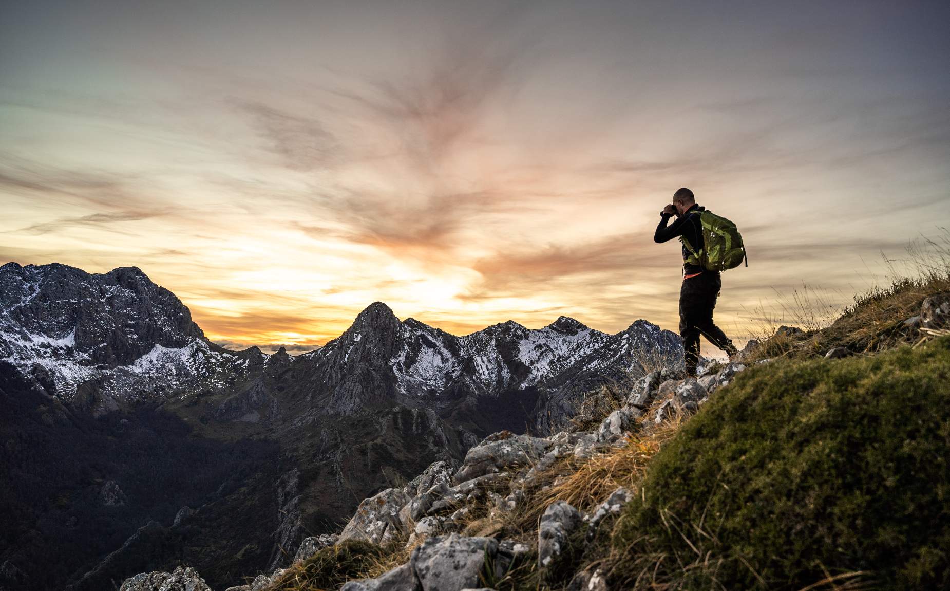 Man walking along the top of a mountain while taking a photograph of the horizon.