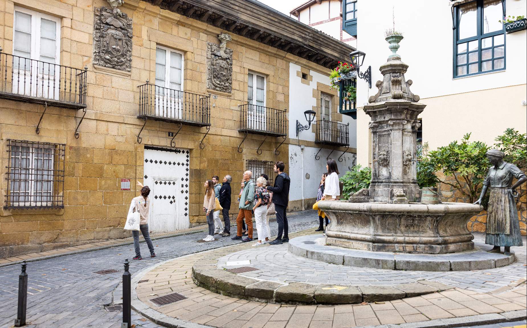 Turistas visitando una plaza de un pueblo con una fuente 
