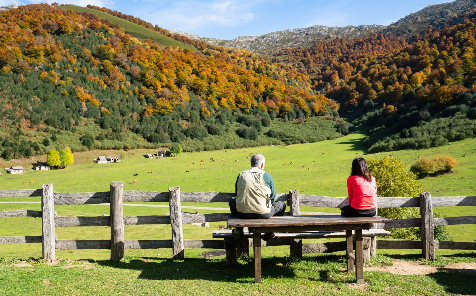Two people sitting on a bench looking out over the countryside and mountains