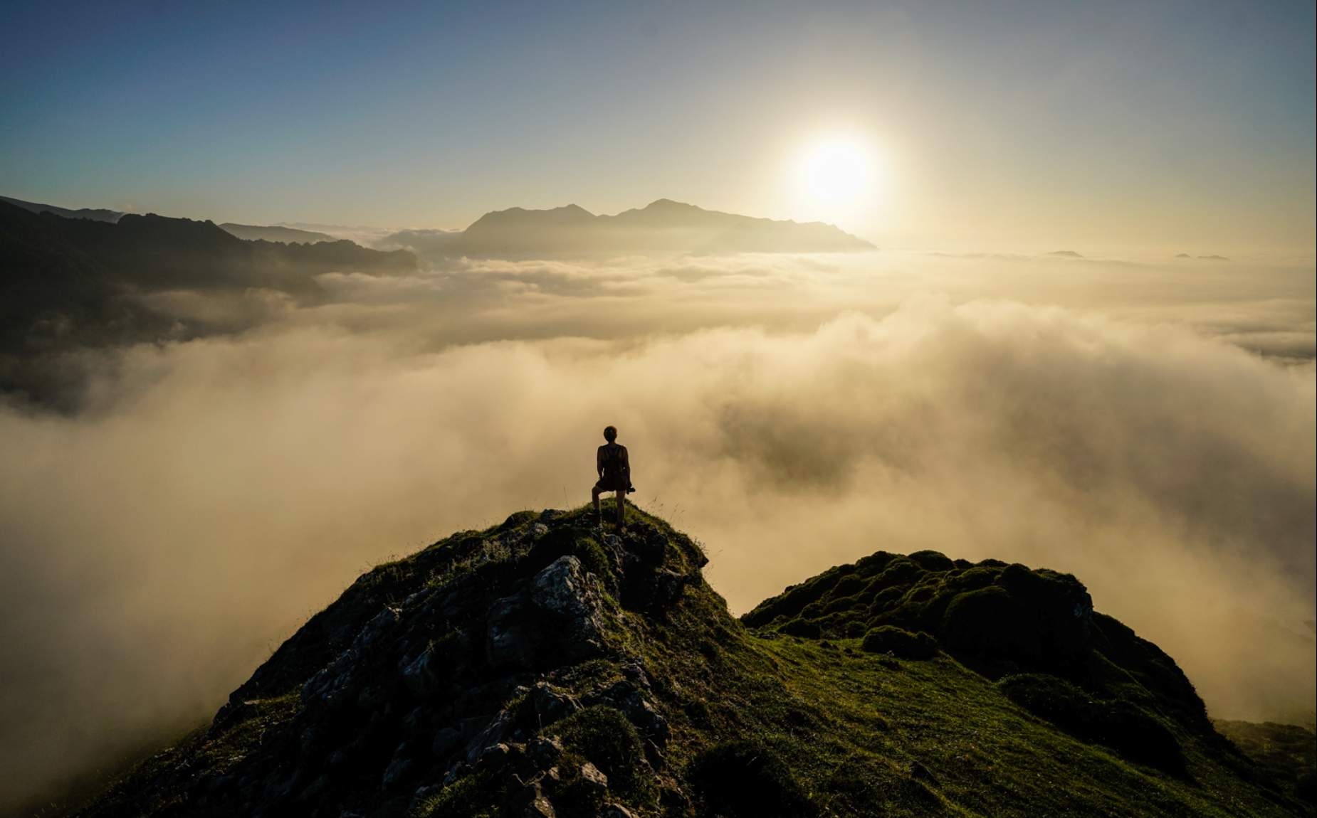 A girl on the top of a mountain looking at the landscape with low clouds.