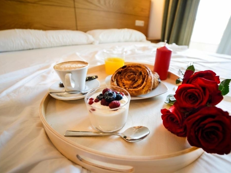 bandeja de desayuno encima de la cama de una habitación con varias rosas rojas