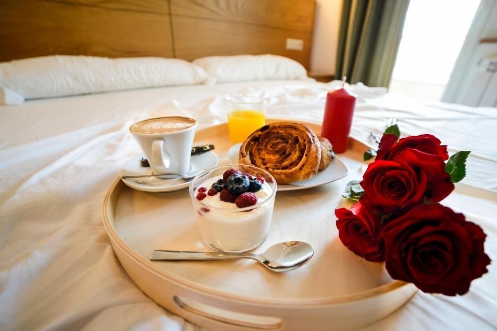 bandeja de desayuno encima de la cama de una habitaci&oacute;n con varias rosas rojas